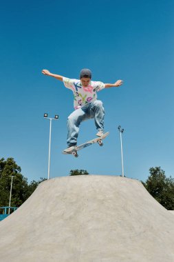 A young skater boy defies gravity, soaring through the air on his skateboard at a sunlit skate park. clipart