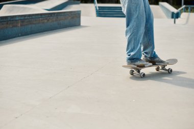 A young skater boy confidently riding his skateboard on top of a cement ramp at a bustling outdoor skate park on a sunny summer day. clipart