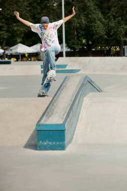 A young skater boy rides his skateboard up the steep side of a ramp in a vibrant outdoor skate park on a sunny summer day. clipart