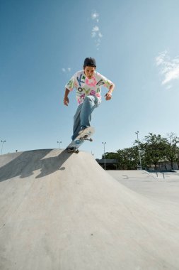 Young skater boy rides skateboard down side of outdoor ramp in summer skate park. clipart