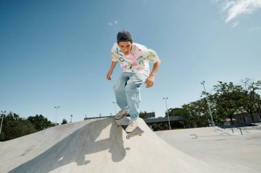 A young skater boy performing an impressive skateboarding trick down the side of a ramp in a sunny outdoor skate park. clipart