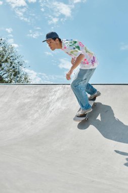 A daring young skater boy rides his skateboard up the side of a ramp in a sunny outdoor skate park on a summer day. clipart