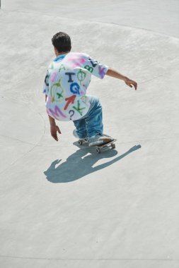 A young skater boy confidently rides a skateboard down a cement ramp in a vibrant outdoor skate park on a sunny summer day. clipart