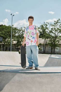 A young man enjoying a summer day at a vibrant skate park, holding a skateboard and ready for a ride. clipart