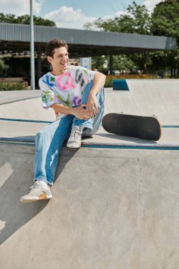 A young man sits pensively on the edge of a skateboard ramp, soaking in the thrill of the impending descent at a skate park. clipart