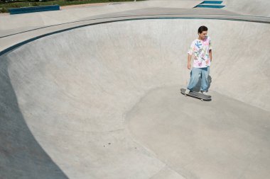 A young man skillfully rides his skateboard at a vibrant skate park on a sunny summer day, showcasing his tricks and talent. clipart