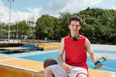 Kırmızı tişörtlü bir adam basketbol sahasının yanında oturmuş huzurlu bir anın tadını çıkarıyor..