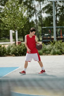Genç bir adam elinde bir topla basketbol sahasında duruyor, yaz güneşinin altında oynamaya hazır..