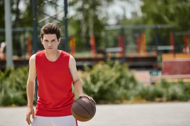 A young man in a vibrant red shirt shows off his basketball skills outdoors on a sunny summer day. clipart