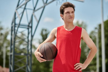 Canlı kırmızı gömlekli genç bir adam bir yaz günü dışarıda oynarken bir basketbol topunu ustalıkla tutuyor..