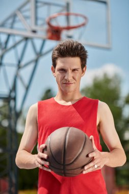 A young man in a red shirt skillfully dribbles a basketball outside on a sunny summer day. clipart
