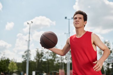 Canlı kırmızı tişörtlü genç bir adam güneşli bir yaz gününde basketbol yeteneklerini sergiliyor..