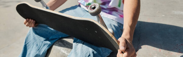 Молодой скейтбордист держит скейтборд в руках в солнечном открытом скейтпарке летом.