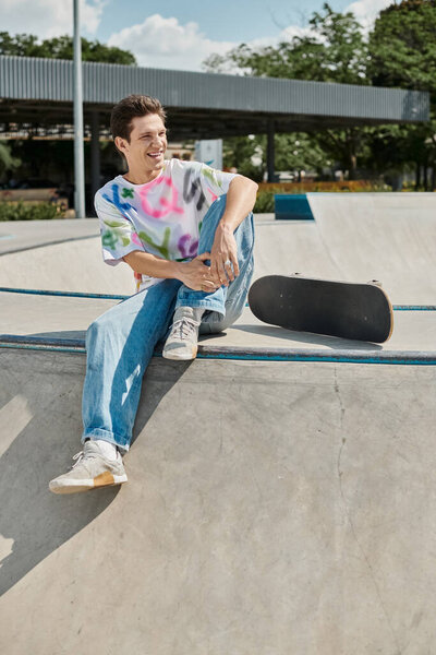 A young man sits pensively on the edge of a skateboard ramp, soaking in the thrill of the impending descent at a skate park.