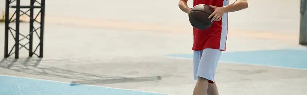 若いバスケットボール選手がバスケットボールコートの上に立って 晴れた夏の日に確信を持ってボールを保持します — ストック写真