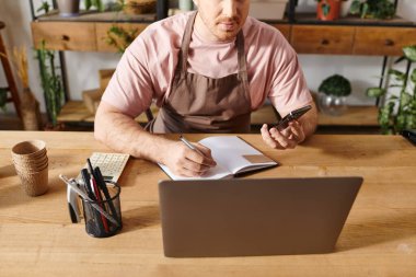 A man sitting at a table with a notebook and pen, brainstorming ideas for his plant shop business. clipart