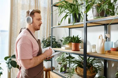 A man in headphones surrounded by lush green plants in a small shop. clipart