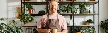 A man stands confidently in front of a shelf full of lush potted plants, showcasing his expertise in floristry and small business ownership. clipart