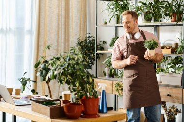 A handsome man in an apron proudly holds a potted plant in a plant shop, showcasing his love for greenery. clipart
