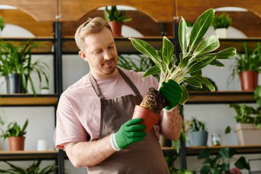 A man in an apron cradles a flourishing potted plant, showcasing his passion for nurturing botanical beauty in his plant shop. clipart