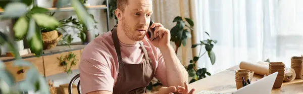 stock image A man in a plant shop, sitting at a table, engaged in a phone call.