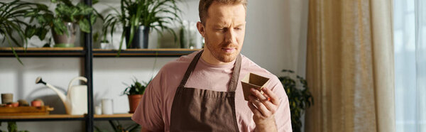 A handsome man in an apron holding a pot for plant, embodying the essence of a small business owner.