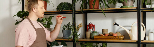 Handsome man stands proudly in front of a shelf filled with various potted plants in his own plant shop.