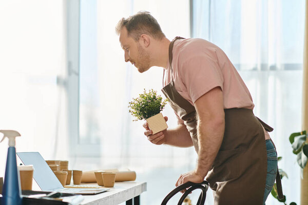 A man tends to a potted plant while working on his laptop, symbolizing virtual growth in his plant shop business.
