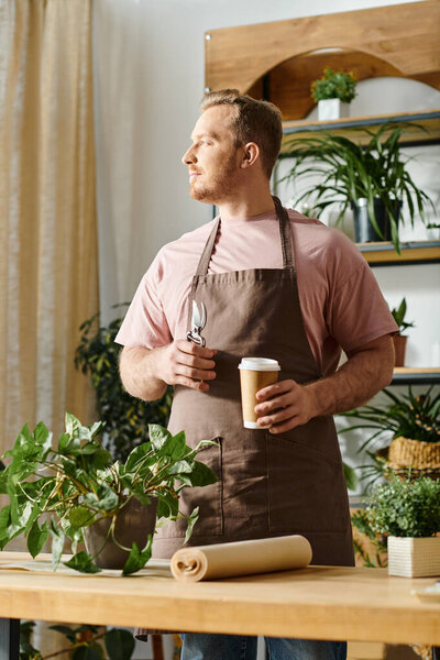 A man in an apron enjoys a moment of relaxation, holding a cup of coffee in a plant shop.