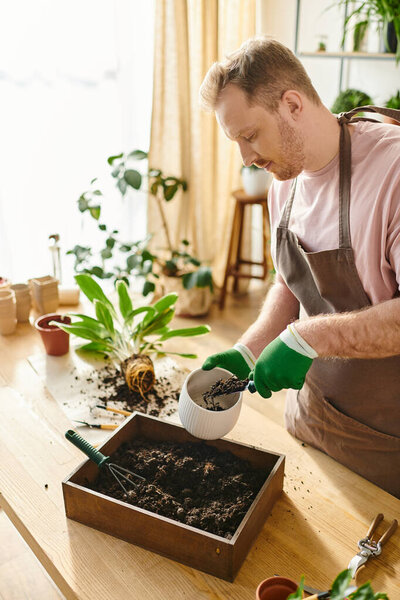 A man in an apron and gloves pours dirt into a container, tending to his plants in a small business plant shop.