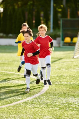 Bir grup genç çocuk, enerji ve heyecan dolu, birlikte eğlenceli bir oyun oynarken futbol sahasında koşuyorlar..