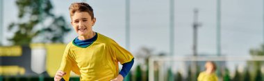 Sahada çeviklik ve kararlılık gösteren, parlak sarı ve mavi futbol üniformalı genç bir adam topa hassasiyetle vuruyor..