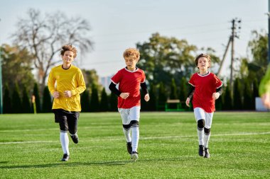 Futbol kıyafeti giymiş genç çocuklardan oluşan canlı bir grup kararlı ve heyecanlı bir şekilde yeşil bir futbol sahasında koşuşturuyorlar..