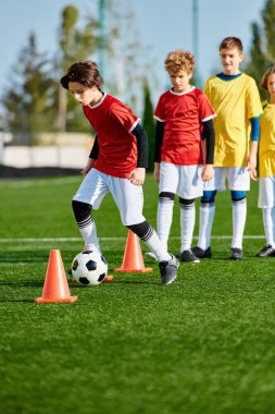 Bir grup genç çocuk enerjik bir şekilde futbol oynuyor, koşuyor, tekmeliyor ve çimenli bir alanda gülüyor. Bazı çocuklar topa vururken, diğerleri gol atmaya çalışıyor. Oyun heyecan ve takım çalışmasıyla dolu..