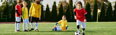 Renkli formalar giyen canlı bir grup çocuk çimen tarlasında enerjik bir şekilde futbol oynuyor. Güneş arka planda batarken koşuyor, tekmeliyor ve şevkle pas atıyorlar..