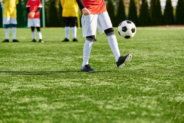 Genç bir adam enerjik bir şekilde canlı bir sahada futbol topunu tekmeliyor. Spordaki becerisini ve çevikliğini gösteriyor..