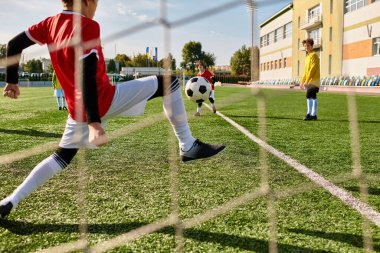 Renkli formalı bir grup çocuk güneş ışığında futbol oynuyor, topu kovalıyor, top sürüyor, pas veriyor ve geçici hedeflere doğru atıyorlar, tomurcuklanan takım çalışması ve bulaşıcı kahkahalarla havayı dolduruyorlar..