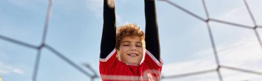 Neşeli genç bir çocuk renkli bir voleybol ağında baş aşağı asılı duruyor. Maceracı ruhunu ve eşsiz aktivitelere olan sevgisini sergiliyor..
