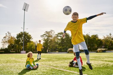 Bir grup genç adam enerjik bir şekilde yeşil bir alanda futbol oynuyor, topa vuruyor, koşuyor ve azimle tezahürat yapıyor..