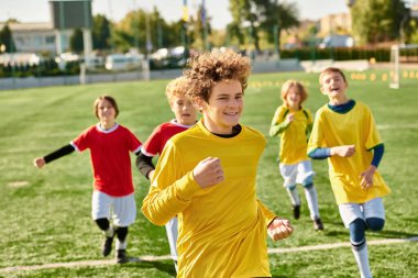 A lively group of young boys joyfully running around a soccer field, kicking the ball, laughing, and chasing each other in friendly competition. clipart