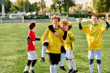 Bir grup genç, başarılı bir maçın ardından yüzleri mutluluk ve gururla ışıldayarak dikkatle manikürlü bir futbol sahasının tepesinde muzaffer bir şekilde ayakta duruyor..