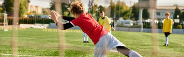 Canlı bir grup genç, parlak güneşin altındaki yeşil bir sahada coşkulu bir futbol maçına katılıyor. Odaklanmış ifadeleri ve hızlı hareketleri, takım çalışmasının ve rekabetin canlandırıcı bir sahnesini oluşturuyor..
