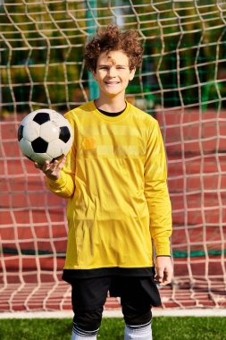 A young man stands in front of a goal, holding a soccer ball in his hands, ready to take a shot, with determination in his eyes. clipart