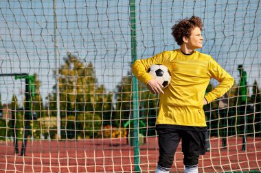 Canlı sarı tişörtlü bir adam futbol topunu kendine güvenle tutuyor ve spora olan tutkusunu gösteriyor..