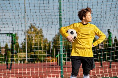 A man in a vibrant yellow shirt confidently holds a soccer ball, showcasing his passion for the sport. clipart