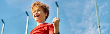A boy in a vibrant red shirt confidently holds a baseball bat with a determined expression. He stands ready, showcasing his passion for the sport and readiness to swing. clipart