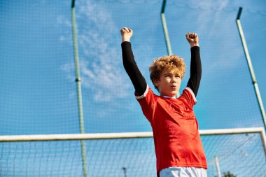 Genç bir çocuk tenis kortunda elinde bir tenis raketi ile güvenle duruyor. Odaklanmış ve oyun oynamaya hazır görünüyor..