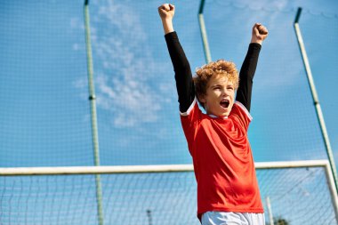 Genç bir çocuk tenis kortunda elinde bir tenis raketi tutarak güvenle duruyor. Odaklanmış bakışları, topa hizmet etmeye ya da karşılık vermeye hazırlanırken oyuna olan kararlılığını ve tutkusunu gösteriyor..