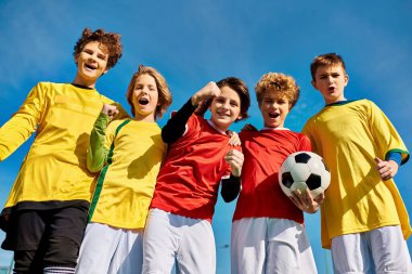 Genç bireylerden oluşan canlı bir grup, bir futbol topunu coşkuyla ve arkadaşlıkla tutarak birbirlerine yakın duruyorlar. Arkadaşça bir oyuna hazırlanırken yüzleri heyecan ve birliği yansıtıyor..