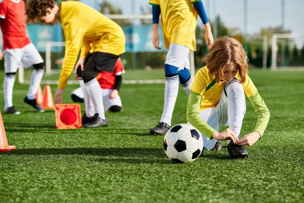 Renkli formalar giyen bir grup genç çocuk enerjik bir şekilde bir sahada futbol oynuyor. Koşuyorlar, topa vuruyorlar ve heyecanla tezahürat yapıyorlar..